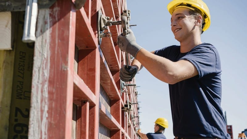 Junger Mann mit Bauhelm arbeitet an Betonrohbau